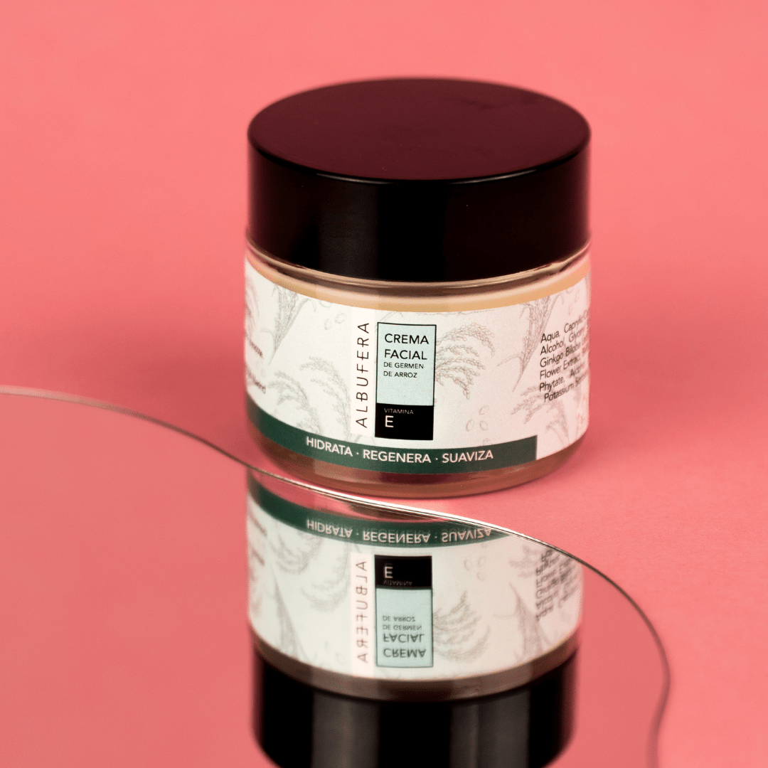 Crema facial de germen de arroz Albufera en su envase sobre un fondo rosa y frente a un espejo