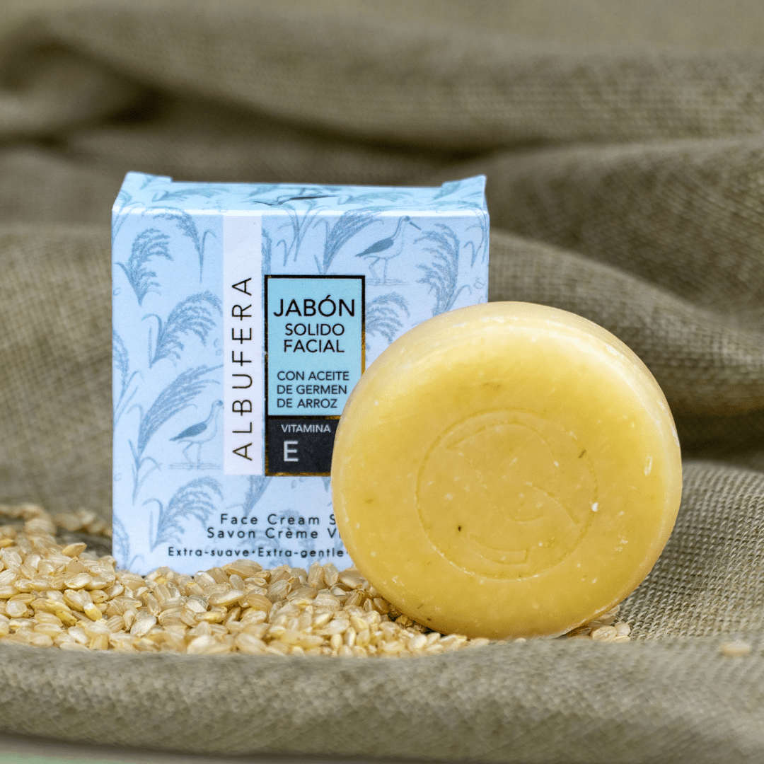 Pastilla de jabón sólido facial Albufera junto a su caja , sobre un sao de granos de arroz